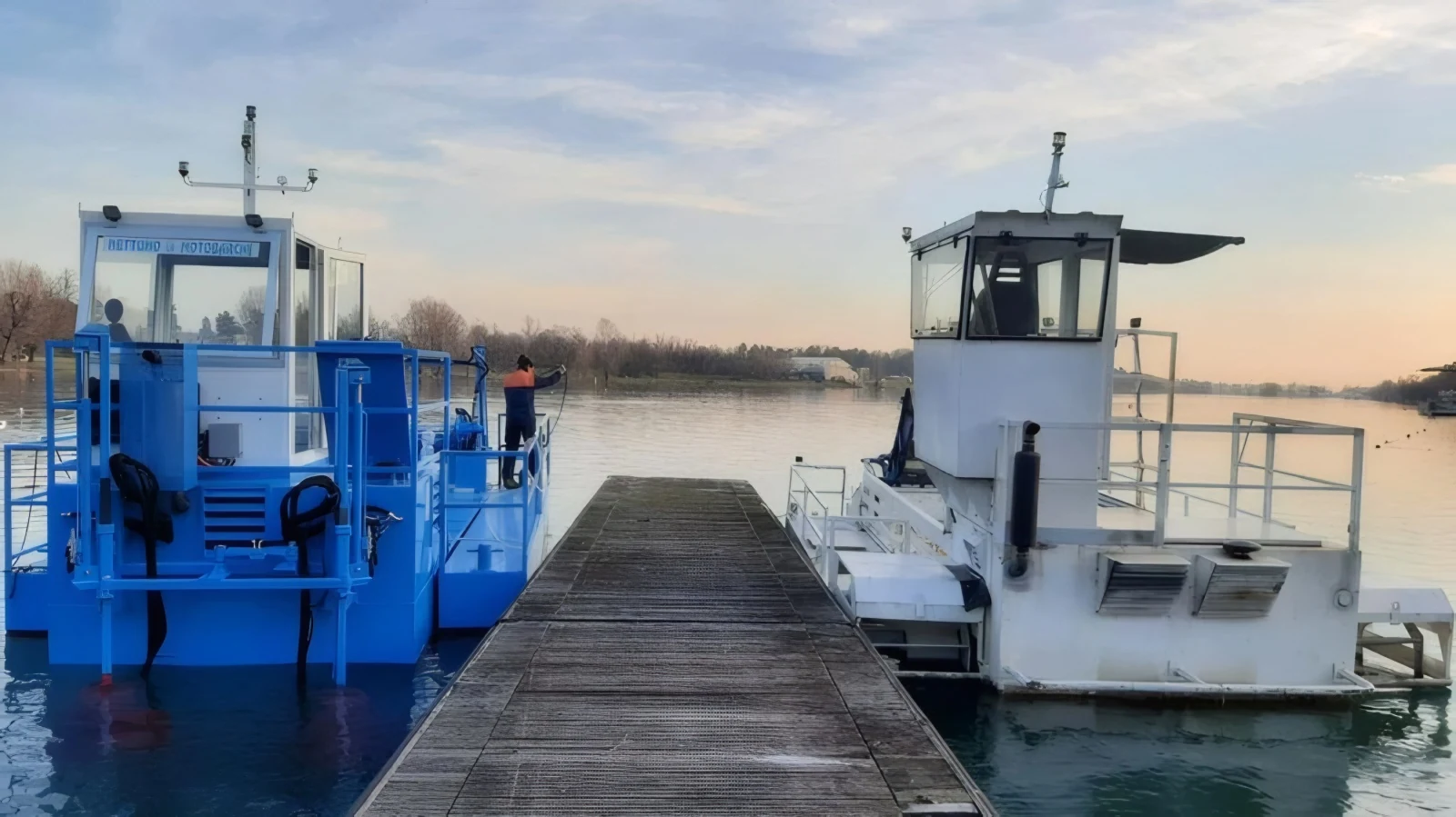 Two Nettuno CHUB aquatic weed harvesters moored at the jetty at sunset